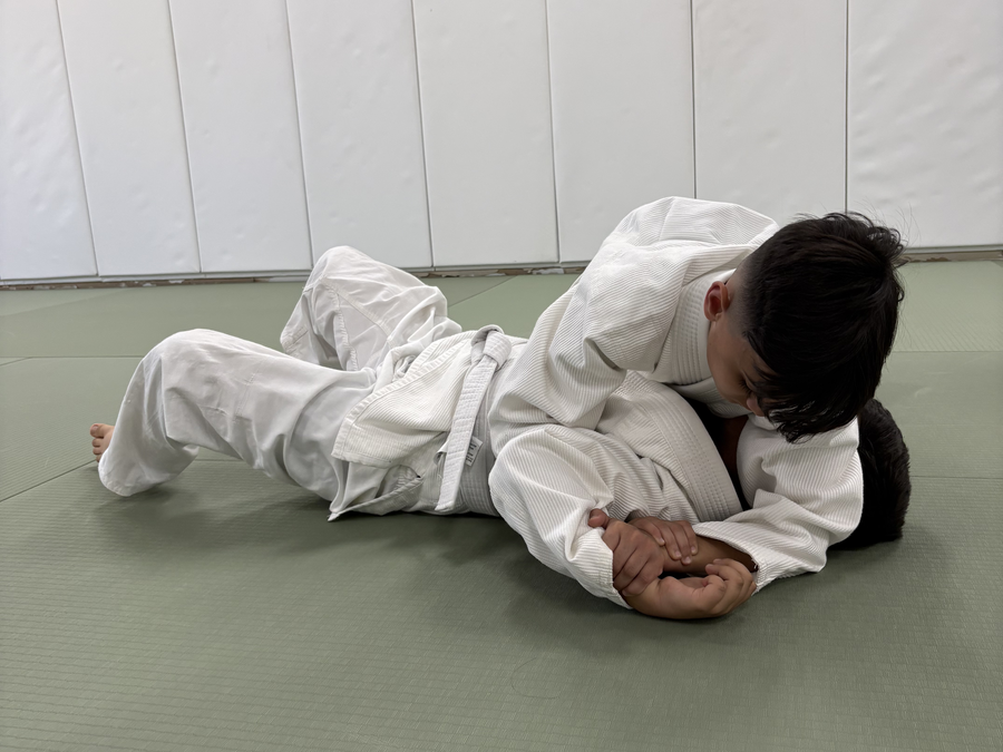 Young student in a white Gi holding side control on the mat during a kids Brazilian Jiu-Jitsu class at Makoto Jiu Jitsu Academy in Turlock, California